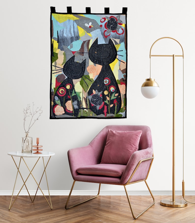 Pode incluir: Um painel de parede com duas silhuetas de gatos pretos e desenhos florais coloridos. O fundo &eacute; uma mistura de cores, incluindo azul, amarelo e cinza. O painel retangular tem abas pretas na parte superior. Decora&ccedil;&atilde;o de casa.