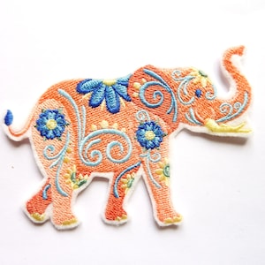 Op de afbeelding: Een geborduurde strijkpatch met een oranje olifant met blauwe en gele bloemenmotieven. De olifant heeft een opgerolde slurf en loopt.
