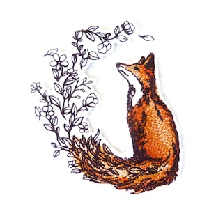 Peut inclure: Un patch brodé représentant un renard à la queue touffue assis dans un cercle de fleurs stylisées. Le renard est orange et brun, et les fleurs sont noires.