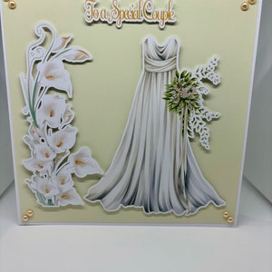 Hermosa tarjeta de boda para una pareja especial. Adornada con vestido de novia, perlas de parte posterior plana y lirios.