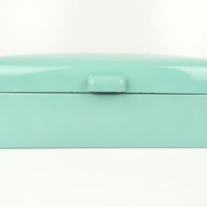 May include: A rectangular bread box with a smooth, glossy mint green finish. The container features a rounded top lid with a small, centered handle tab for opening. The design is simple and clean, showcasing a solid pastel color throughout.