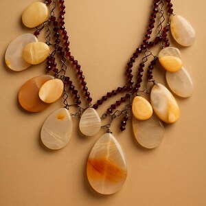 May include: A statement necklace featuring large, teardrop-shaped pendants in shades of yellow and orange. The pendants are strung on a chain with small, dark red beads. The necklace has a layered design and a unique, eye-catching appearance.