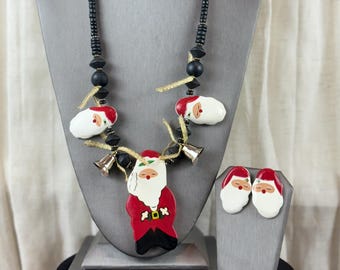 May include: A Christmas-themed necklace and earring set. The necklace features a Santa Claus pendant with a red coat, black pants, and a white beard. The earrings are Santa Claus faces. The necklace is 18 inches long.