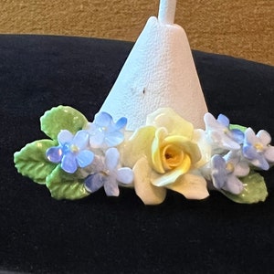 Op de afbeelding: Een witte keramische basis met een gele roos en blauwe bloemen. De basis is kegelvormig en heeft een klein gaatje bovenaan.