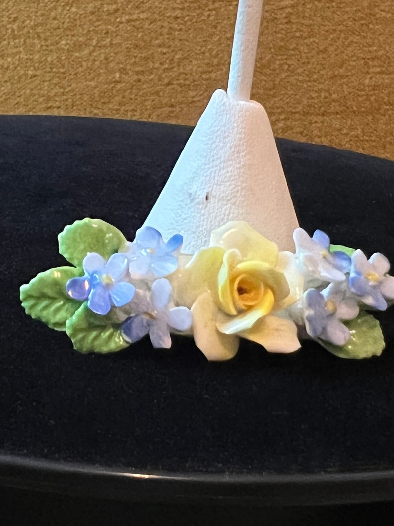 Op de afbeelding: Een witte keramische basis met een gele roos en blauwe bloemen. De basis is kegelvormig en heeft een klein gaatje bovenaan.