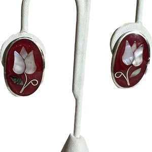 May include: A pair of silver earrings with a red oval background and a white mother of pearl tulip design.