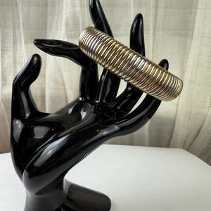 May include: A silver and gold expandable bangle bracelet with a ribbed design.
