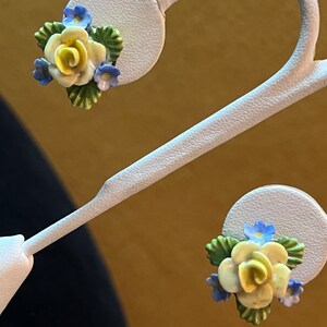 Op de afbeelding: Een paar gele en blauwe bloemen oorbellen. De oorbellen zijn gemaakt van porselein en hebben een delicate roos met blauwe bloemen en groene bladeren.