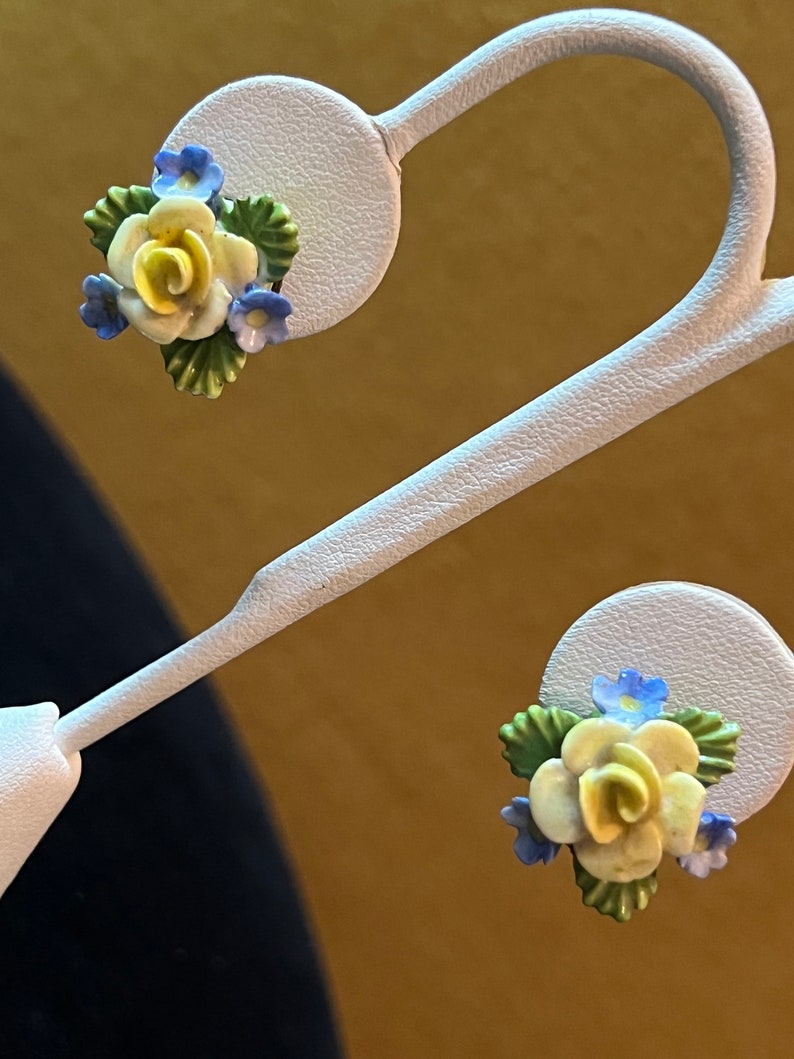 Op de afbeelding: Een paar gele en blauwe bloemen oorbellen. De oorbellen zijn gemaakt van porselein en hebben een delicate roos met blauwe bloemen en groene bladeren.