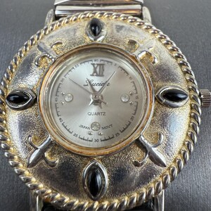 Op de afbeelding: Een zilverkleurig Lucidi quartz horloge met een decoratieve wijzerplaat. Het horloge heeft een zilveren wijzerplaat met Romeinse cijfers en zwarte accenten. De horlogeband is zilver. Het horloge ligt op een grijze ondergrond.
