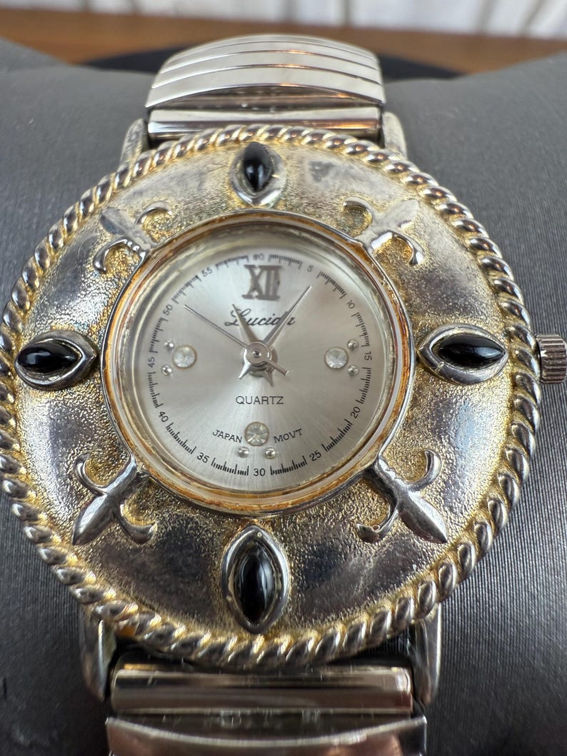 Op de afbeelding: Een zilverkleurig Lucidi quartz horloge met een decoratieve wijzerplaat. Het horloge heeft een zilveren wijzerplaat met Romeinse cijfers en zwarte accenten. De horlogeband is zilver. Het horloge ligt op een grijze ondergrond.