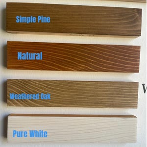 K&ouml;nnte beinhalten: Vier Holzbretter mit Beispielen f&uuml;r Beizfarben: Simple Pine, Natural, Weathered Oak und Pure White. Jedes Brett zeigt die Holzmaserung und den Namen der Beize in blauem Text. Die Bretter sind horizontal vor einem wei&szlig;en Hintergrund angeordnet.