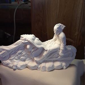 May include: White ceramic figurine of a person riding a motorcycle. The figurine is in a dynamic pose, with the person leaning forward and the motorcycle tilted. The figurine is unpainted and ready to be decorated.