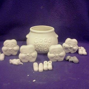 May include: A set of ceramic cookie jar and figurines. The cookie jar is white and has the words "Good Luck" on it. The figurines are white and have smiling faces.