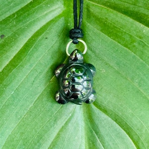 May include: A black obsidian turtle pendant on a black cord necklace. The pendant is polished and has a shiny finish.