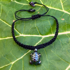 May include: Black braided cord bracelet with a black hematite turtle charm.