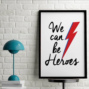 May include: A black framed print with a white background and the text "We can be Heroes" in black cursive writing. A red and blue lightning bolt graphic is to the right of the text.