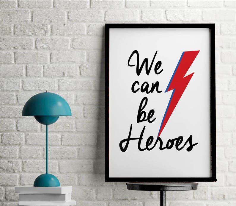 May include: A black framed print with a white background and the text "We can be Heroes" in black cursive writing. A red and blue lightning bolt graphic is to the right of the text.