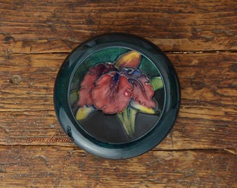May include: A round ceramic trinket box with a dark green background and a colourful orchid flower design.