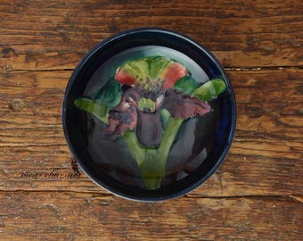 May include: A blue ceramic dish featuring a colourful floral design. The flower is a vibrant red, green and purple iris.