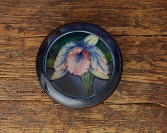May include: A blue ceramic trinket dish featuring a raised floral design of a pink and white orchid. The dish has a dark blue glaze and a glossy finish.