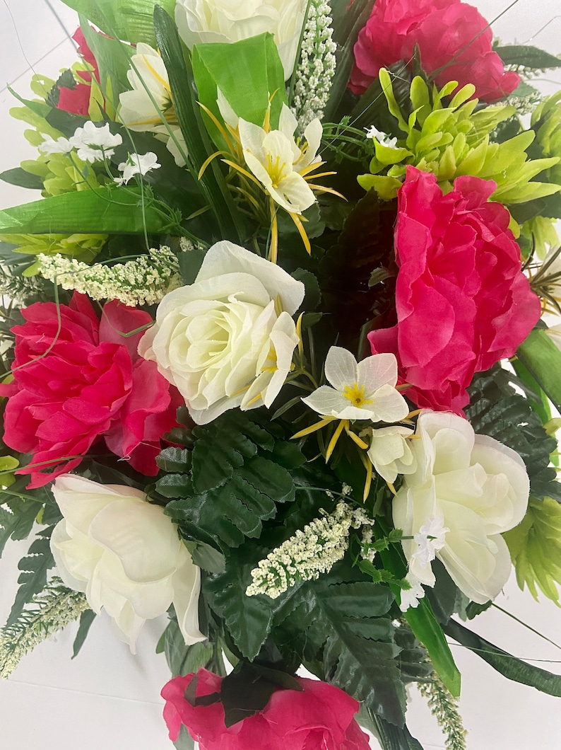 May include: A bouquet of artificial flowers with white roses, pink peonies, and green foliage.