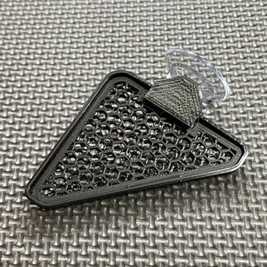 May include: Black triangular shaped suction cup with a honeycomb pattern. The suction cup is designed to hold a small object.