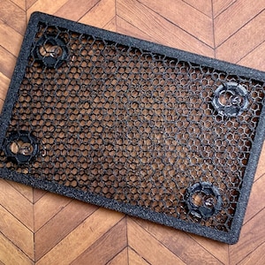 Peut inclure: Un treillis métallique noir rectangulaire avec un motif en nid d'abeille. Quatre fixations circulaires sont espacées uniformément sur le treillis. Le treillis est posé sur une surface en bois.