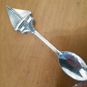 May include: Silver teaspoon with a sailboat design on the handle. The sailboat has the text "America's Cup 1987" on it.