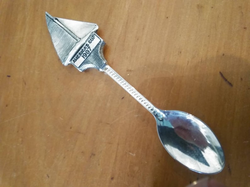 May include: Silver teaspoon with a sailboat design on the handle. The sailboat has the text "America's Cup 1987" on it.