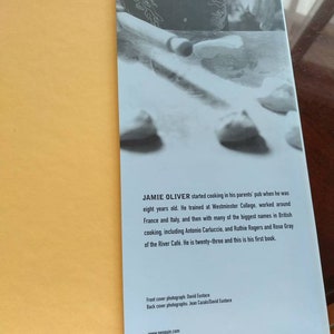 Puede incluir: Una portada de libro con una foto de un chef haciendo masa. El libro se titula "Jamie Oliver" y es su primer libro de cocina. El texto de la contraportada describe su trayectoria culinaria, incluyendo su formaci&oacute;n en el Westminster College y su trabajo con chefs famosos como Antonio Carluccio.