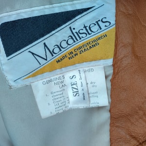Puede incluir: Una etiqueta blanca con texto negro que dice "Macalisters Made in Christchurch New Zealand". Debajo del texto hay un tri&aacute;ngulo amarillo. Una etiqueta blanca m&aacute;s peque&ntilde;a con texto negro dice "Genuine S New LAM 1. Garments cleaned cleaners. 2. Clean in 113 only material 3. Hang dry at 40 degrees". Una tercera etiqueta blanca con texto negro dice "Size S Made in New Zealand Shed dry-dry solvent oiling Jumble Conincade".