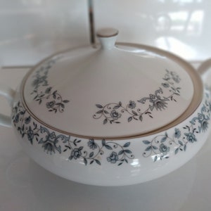 Peut inclure: Plat de service en porcelaine blanche avec un couvercle. Le plat est décoré d'un motif floral noir et bleu avec une bordure dorée.