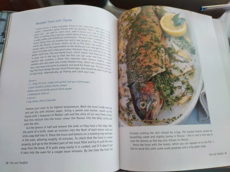 Puede incluir: Una trucha asada con tomillo, lim&oacute;n y hojas de laurel en un plato blanco. La trucha est&aacute; cocinada y tiene una piel crujiente. Los limones est&aacute;n asados y tienen una textura confitada. La receta es para trucha asada con tomillo.