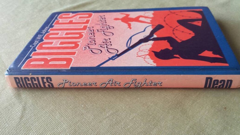 May include: A vintage book titled "Biggles Pioneer Air Fighter" by Capt. W.E. Johns. The cover features a red and blue illustration of a silhouette of a person with a rifle, barbed wire, and a plane. The book's spine is visible.
