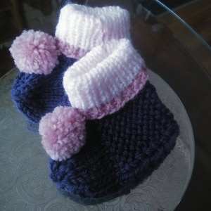 May include: A pair of knitted baby booties with pink pom-poms and a white and pink trim.