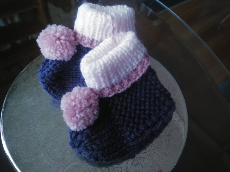 May include: A pair of knitted baby booties with pink pom-poms and a white and pink trim.