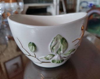 May include: White ceramic bowl with a floral design featuring green leaves and gold accents. The bowl has a rounded shape and a smooth, glossy finish.