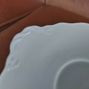 May include: White ceramic saucer with a scalloped edge and a raised design around the rim.