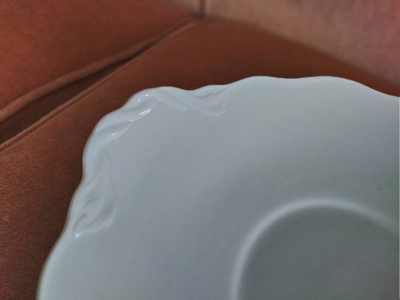 May include: White ceramic saucer with a scalloped edge and a raised design around the rim.