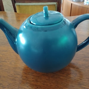 Puede incluir: Una tetera de cer&aacute;mica azul turquesa con cuerpo redondo y tapa. La tetera tiene un pico y una asa.