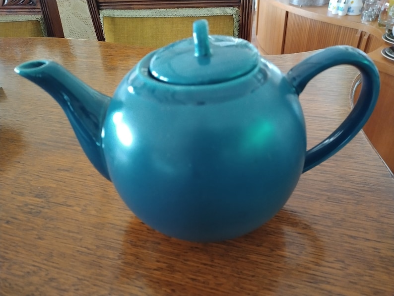 Puede incluir: Una tetera de cer&aacute;mica azul turquesa con cuerpo redondo y tapa. La tetera tiene un pico y una asa.