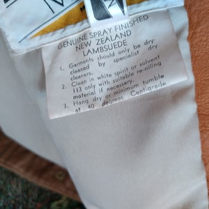 Puede incluir: Etiqueta de cuidado blanca con instrucciones para limpiar el ante de cordero de Nueva Zelanda genuino rociado acabado. La etiqueta dice que solo se debe limpiar en seco por tintorer&iacute;as especializadas, limpiar con alcohol blanco o solvente 113 solo con material de re-aceitado adecuado si es necesario, colgar para secar o m&iacute;nimo de secado en secadora a 40 grados cent&iacute;grados.