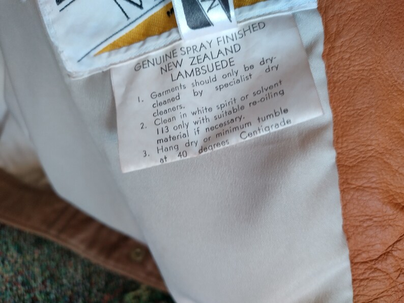 Puede incluir: Etiqueta de cuidado blanca con instrucciones para limpiar el ante de cordero de Nueva Zelanda genuino rociado acabado. La etiqueta dice que solo se debe limpiar en seco por tintorer&iacute;as especializadas, limpiar con alcohol blanco o solvente 113 solo con material de re-aceitado adecuado si es necesario, colgar para secar o m&iacute;nimo de secado en secadora a 40 grados cent&iacute;grados.