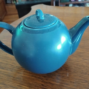 Puede incluir: Una tetera de cer&aacute;mica azul turquesa con cuerpo redondo y tapa. La tetera tiene un asa y un pico.