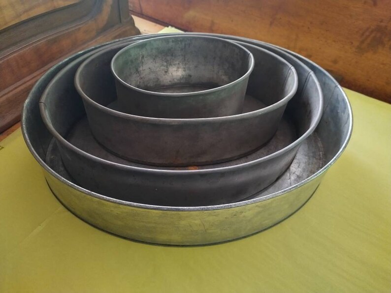 K&ouml;nnte beinhalten: Ein Satz von vier ineinander verschachtelten, runden Kuchenformen aus Metall. Die Formen sind unterschiedlich gro&szlig;, wobei die gr&ouml;&szlig;te Form unten und die kleinste Form in der Mitte liegt. Das Metall hat eine stumpfe, silbergraue Farbe.