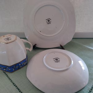 Puede incluir: Un juego de taza y platillo de t&eacute; blanco con un patr&oacute;n floral azul y dorado. La parte inferior del platillo y la taza de t&eacute; tienen impresas las palabras "Royal Albert, Crown China, England" en negro.