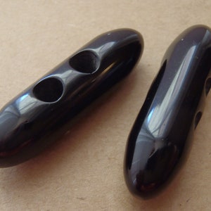 May include: Two black plastic toggle buttons with two holes each. The buttons are oval shaped and have a glossy finish.