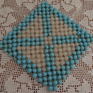 May include: A blue and white beaded trivet, made of small round beads, in a diamond shape.