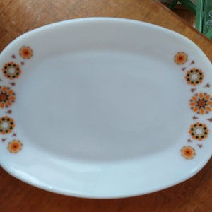 May include: White oval serving platter with a decorative floral pattern in orange, brown, and black. The pattern is arranged along the edges of the platter. A vintage piece for serving food.